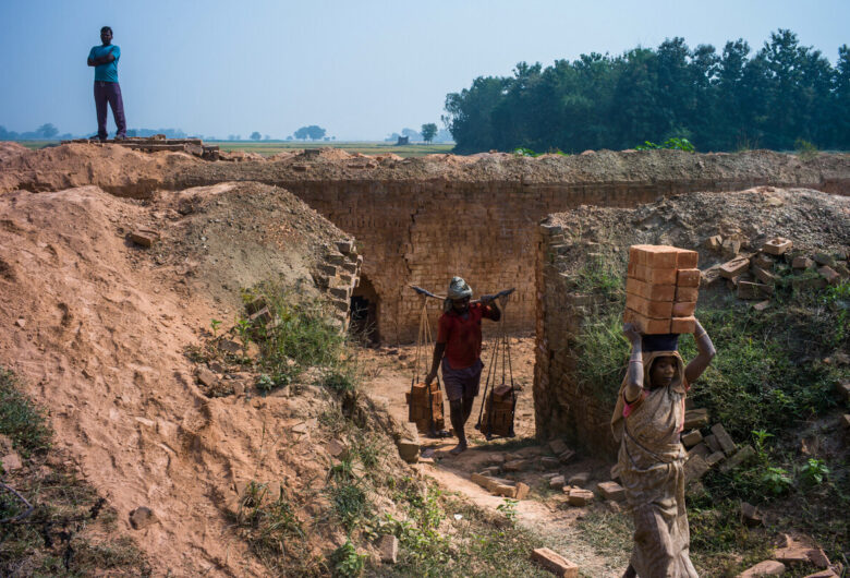A supervisor keeps an eye on the daily wage labourers as they carry a load of bricks in the brick kiln in Baruhuaa village in Chandauli district of Uttar Pradesh, India. The workers are entitled to get INR180 ($3) per 1000 bricks but the contractor only gives INR 80 - INR 100 ($1.25 - $1.7). Photo: Sanjit Das